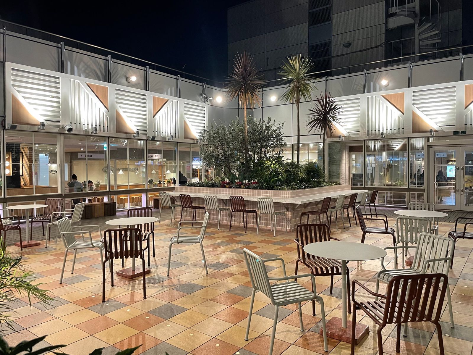 A rooftop garden terrace at night with a central planting bed, tiled floor and slatted wall panels