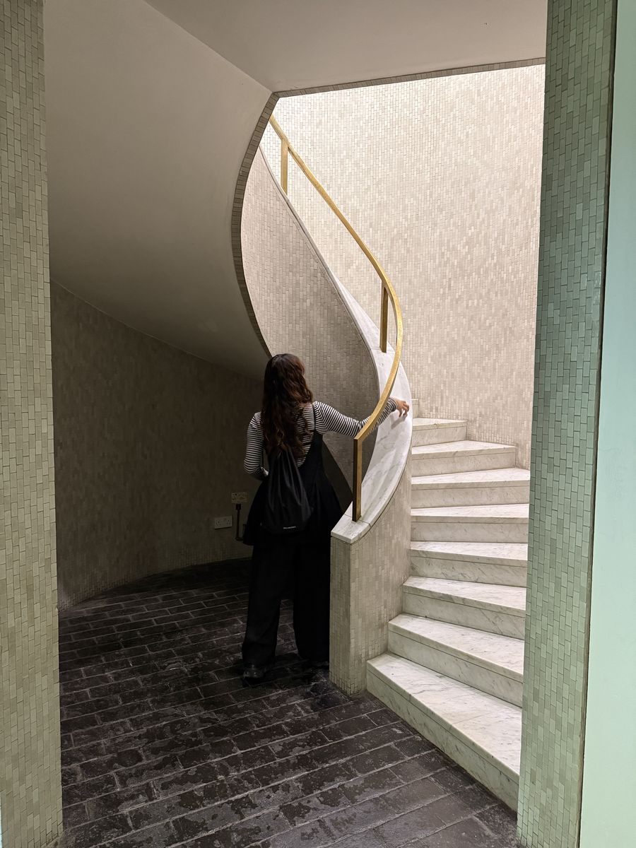Miho Furuwa beside a spiral marble staircase with a brass handrail